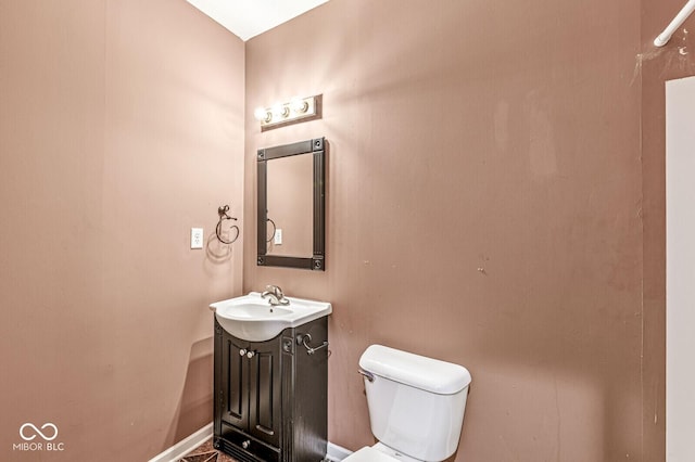 half bathroom featuring toilet, baseboards, and vanity