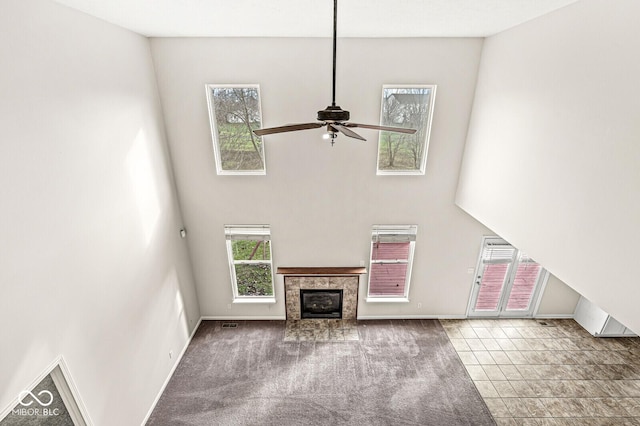 unfurnished living room featuring carpet, a high ceiling, a tiled fireplace, and baseboards