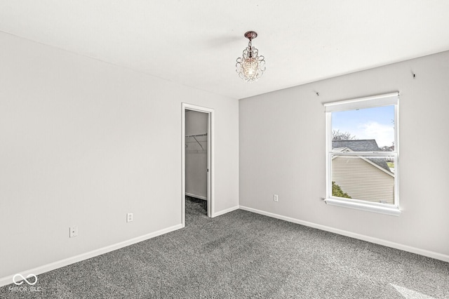 unfurnished bedroom with baseboards, an inviting chandelier, a walk in closet, carpet flooring, and a closet