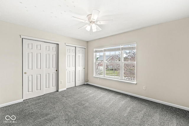 unfurnished bedroom with carpet floors, a ceiling fan, baseboards, and two closets