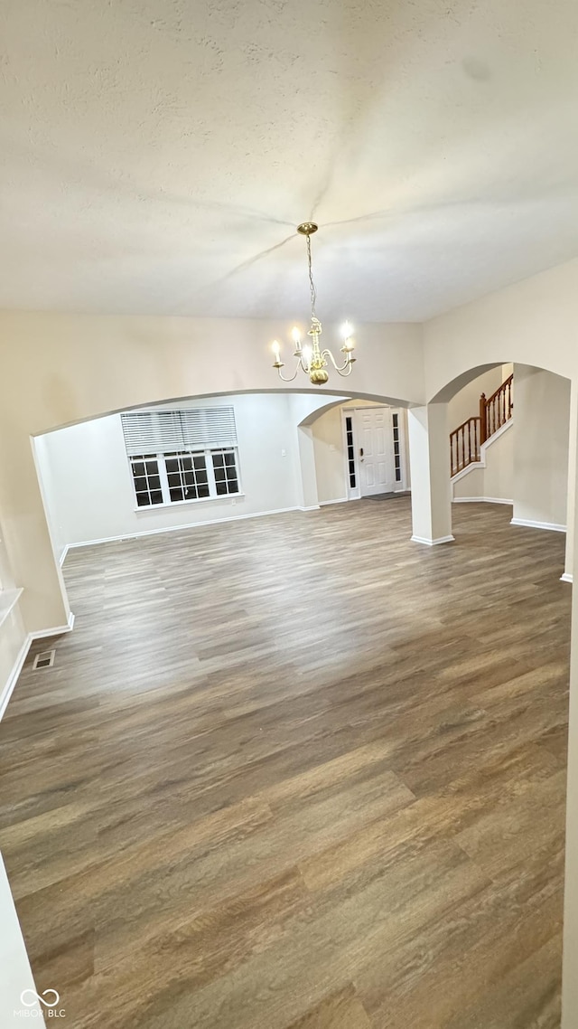 unfurnished living room featuring baseboards, arched walkways, wood finished floors, an inviting chandelier, and stairs