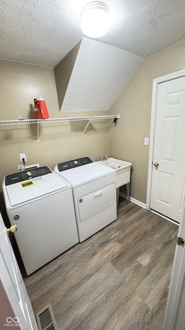 clothes washing area with laundry area, wood finished floors, a textured ceiling, separate washer and dryer, and a sink