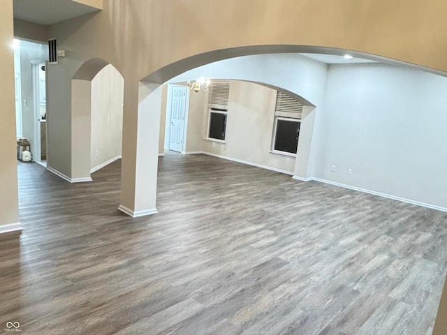 unfurnished living room with arched walkways, wood finished floors, and baseboards