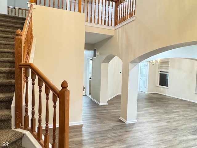 staircase featuring baseboards, arched walkways, wood finished floors, an inviting chandelier, and a high ceiling