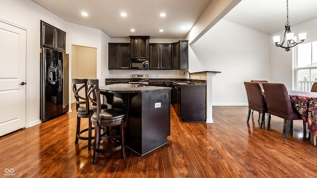 kitchen with dark wood-type flooring, dark stone counters, black appliances, a kitchen breakfast bar, and hanging light fixtures