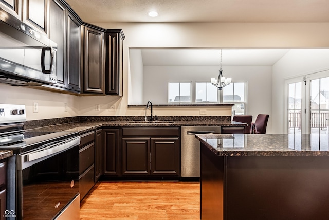 kitchen featuring stainless steel appliances, sink, light hardwood / wood-style flooring, dark stone countertops, and a chandelier