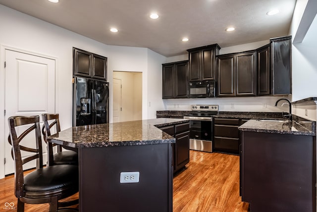 kitchen with sink, dark stone countertops, light hardwood / wood-style floors, a kitchen island, and black appliances