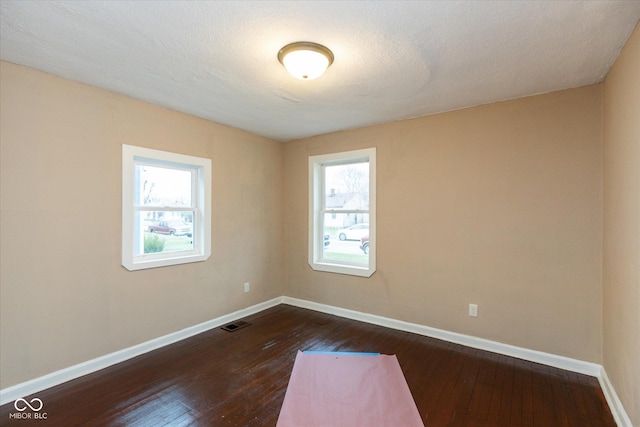 unfurnished room with a healthy amount of sunlight, dark hardwood / wood-style flooring, and a textured ceiling