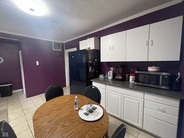 kitchen with black refrigerator, white cabinetry, and light tile patterned floors