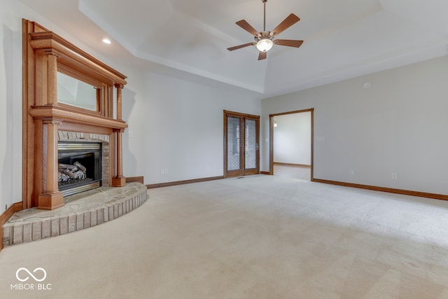 unfurnished living room featuring a fireplace, light colored carpet, a raised ceiling, and ceiling fan