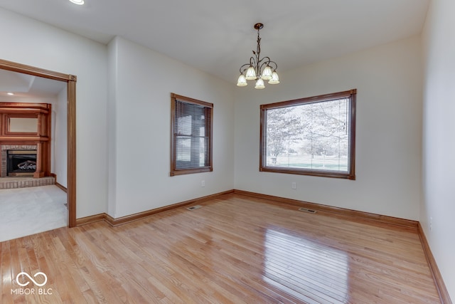 empty room with a fireplace, light hardwood / wood-style flooring, and an inviting chandelier