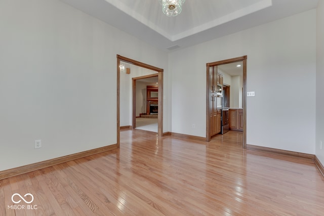 unfurnished room with light wood-type flooring and a tray ceiling