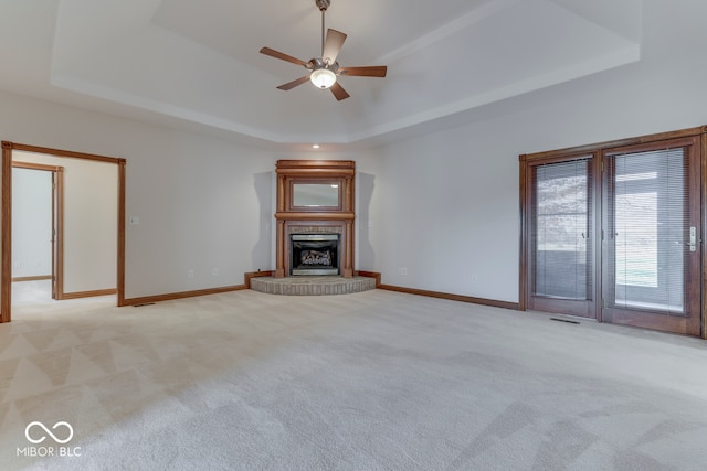 unfurnished living room featuring a raised ceiling, ceiling fan, and light colored carpet