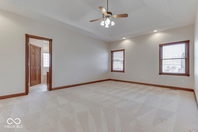 spare room featuring a tray ceiling, ceiling fan, light colored carpet, and a healthy amount of sunlight