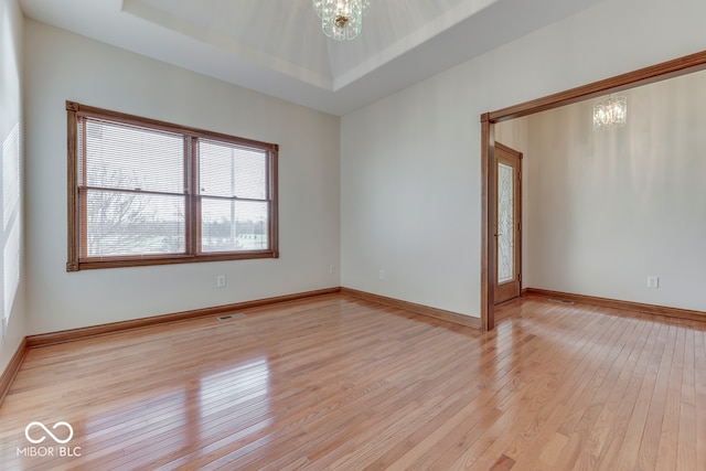 unfurnished room featuring a tray ceiling, light wood-type flooring, and an inviting chandelier