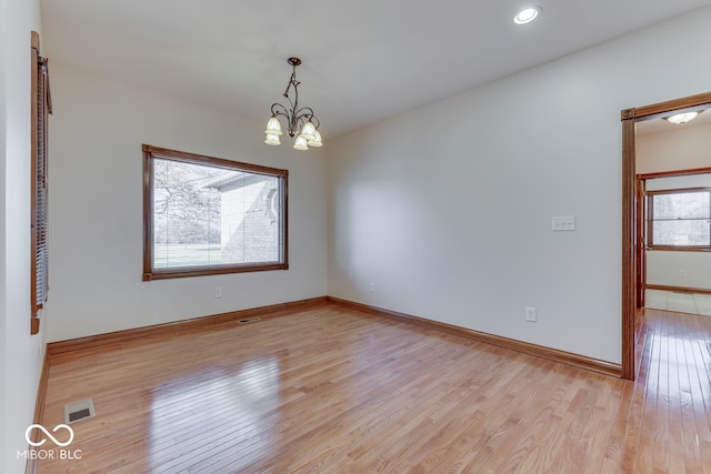 empty room with a notable chandelier and light wood-type flooring