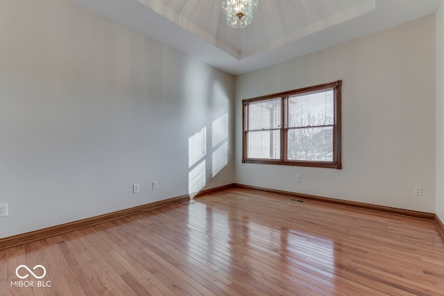 empty room with a notable chandelier, light wood-type flooring, and a tray ceiling