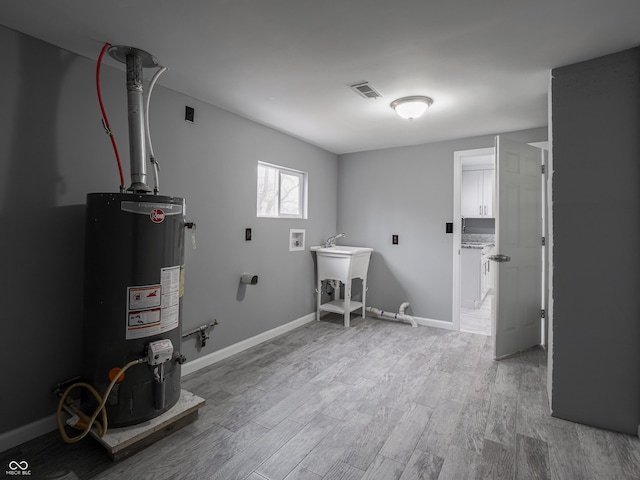 washroom featuring water heater, hookup for a washing machine, light hardwood / wood-style floors, and sink