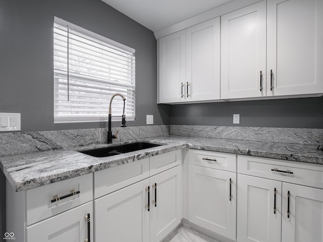 kitchen featuring white cabinets, light stone counters, and sink