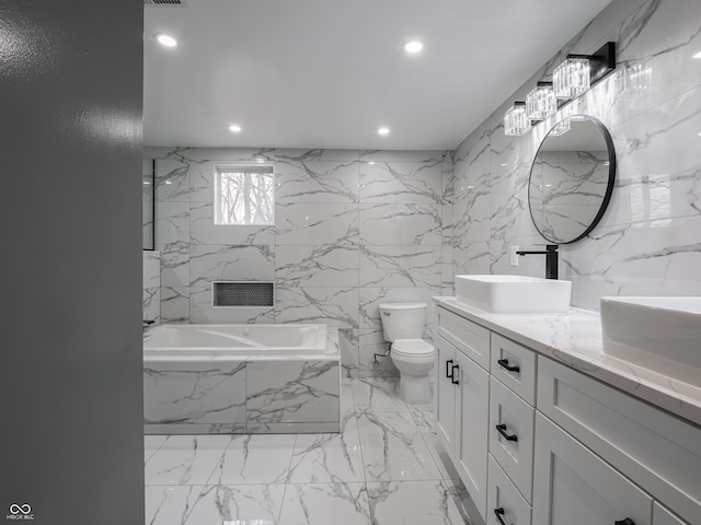 bathroom with vanity, tiled bath, toilet, and tile walls