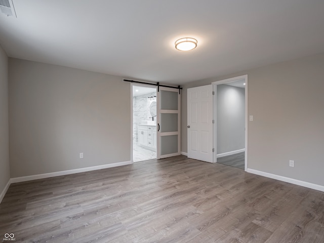 unfurnished bedroom featuring a barn door, ensuite bathroom, and light hardwood / wood-style floors