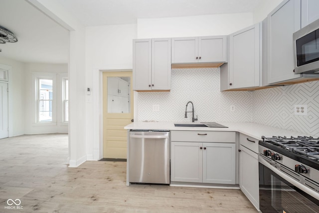 kitchen with decorative backsplash, appliances with stainless steel finishes, light hardwood / wood-style floors, and sink