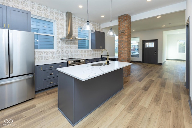 kitchen featuring decorative columns, wall chimney exhaust hood, stainless steel appliances, sink, and hanging light fixtures