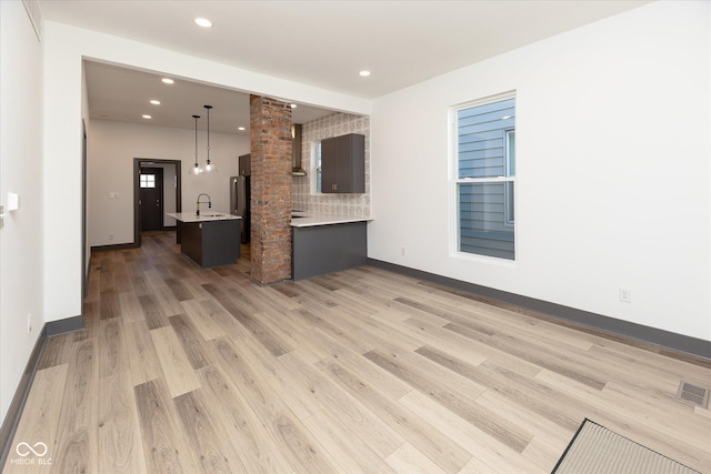 unfurnished living room featuring light hardwood / wood-style floors, ornate columns, and sink