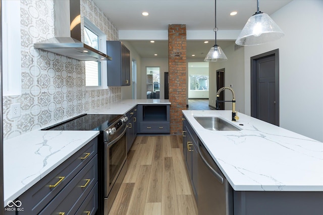 kitchen featuring sink, wall chimney exhaust hood, light hardwood / wood-style floors, decorative light fixtures, and appliances with stainless steel finishes