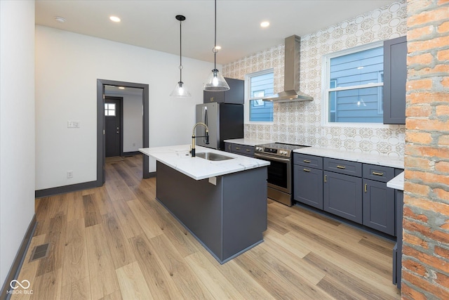 kitchen with appliances with stainless steel finishes, backsplash, wall chimney range hood, light hardwood / wood-style flooring, and an island with sink