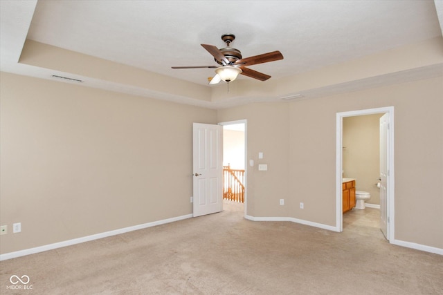 unfurnished bedroom with a raised ceiling, ensuite bath, ceiling fan, and light colored carpet