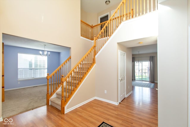 staircase with a chandelier, a towering ceiling, hardwood / wood-style flooring, and a healthy amount of sunlight