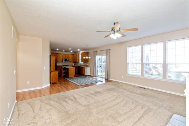 unfurnished living room with a textured ceiling, ceiling fan with notable chandelier, and light wood-type flooring