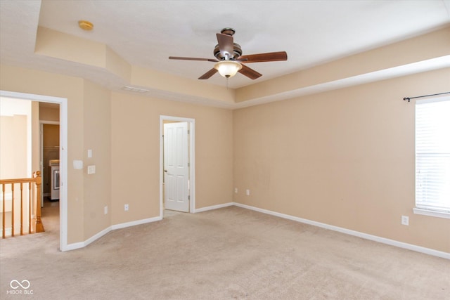 empty room with a raised ceiling, ceiling fan, and light colored carpet