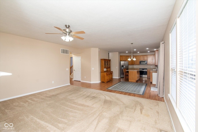 unfurnished living room featuring ceiling fan with notable chandelier and light hardwood / wood-style floors