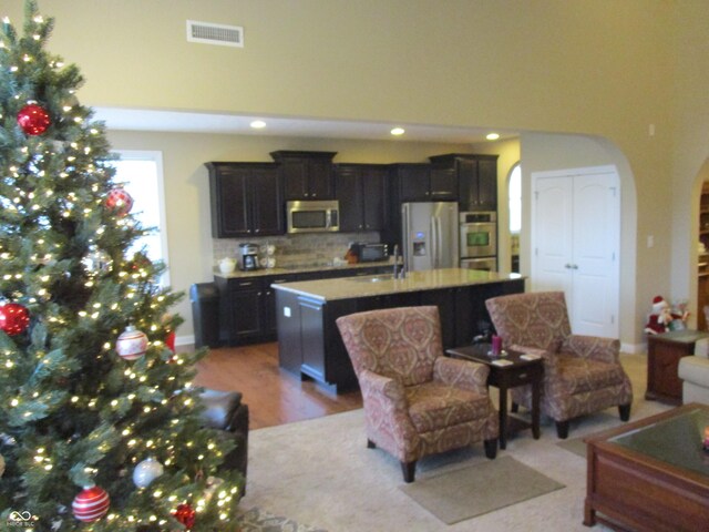 kitchen featuring backsplash, a kitchen island with sink, sink, light wood-type flooring, and appliances with stainless steel finishes