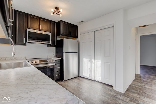 kitchen featuring dark brown cabinetry, sink, light hardwood / wood-style floors, and appliances with stainless steel finishes