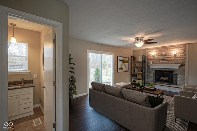 living room with ceiling fan, sink, a stone fireplace, dark hardwood / wood-style flooring, and a textured ceiling