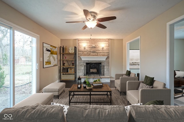 living room featuring a textured ceiling, a stone fireplace, and ceiling fan