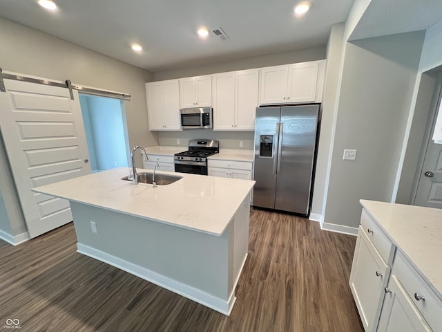 kitchen featuring a center island with sink, white cabinets, sink, a barn door, and appliances with stainless steel finishes