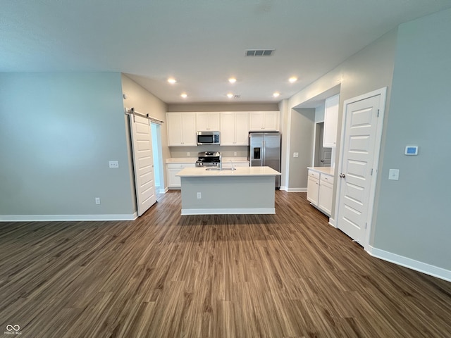 kitchen with a kitchen island with sink, a barn door, dark hardwood / wood-style flooring, white cabinetry, and stainless steel appliances