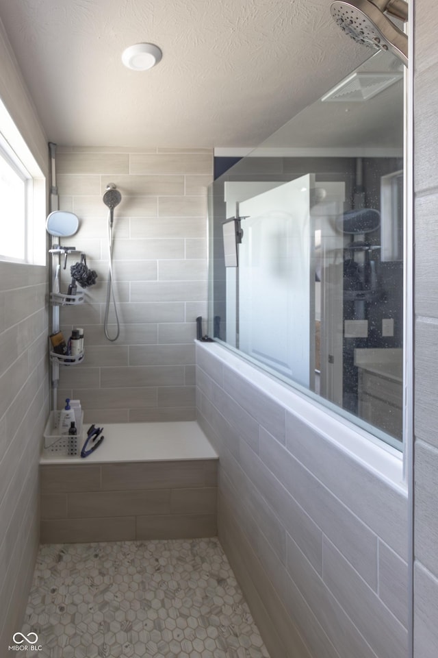 bathroom featuring tiled shower, a textured ceiling, and tile walls