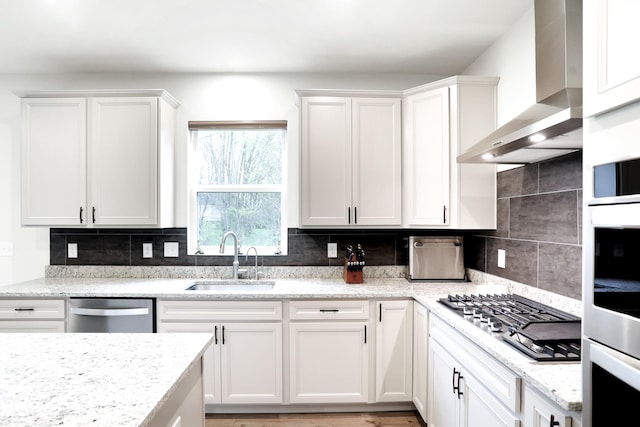 kitchen featuring sink, wall chimney exhaust hood, appliances with stainless steel finishes, tasteful backsplash, and white cabinetry