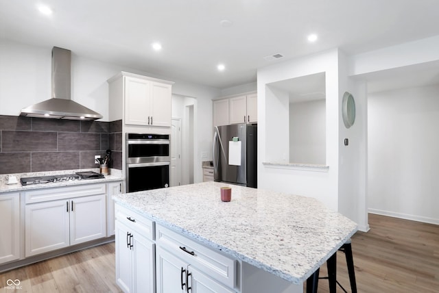 kitchen featuring appliances with stainless steel finishes, light hardwood / wood-style floors, white cabinetry, and wall chimney range hood