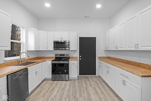 kitchen featuring stainless steel appliances, sink, light hardwood / wood-style flooring, white cabinetry, and butcher block counters