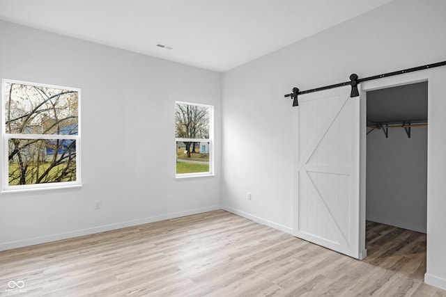 unfurnished bedroom with multiple windows, a walk in closet, light wood-type flooring, and a barn door