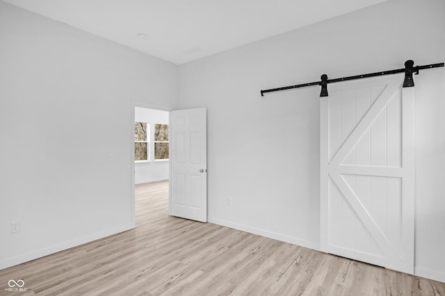 unfurnished bedroom with a barn door and light hardwood / wood-style floors