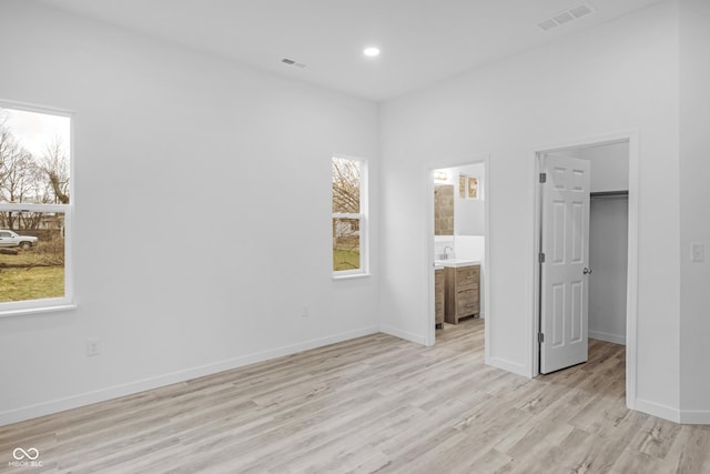 unfurnished bedroom featuring ensuite bath, light hardwood / wood-style floors, a spacious closet, and multiple windows