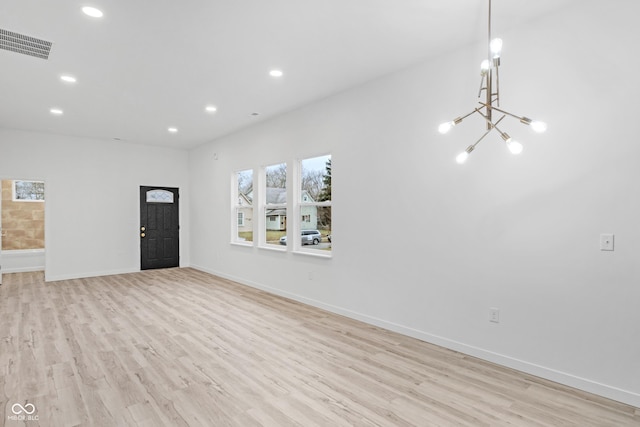 unfurnished living room featuring a notable chandelier and light wood-type flooring