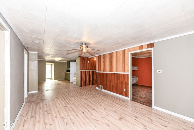 spare room featuring light hardwood / wood-style flooring, ceiling fan, ornamental molding, and wood walls